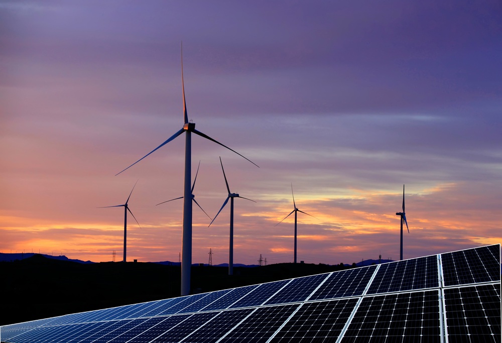 Windräder und Photovoltaik-Panels vor einem Sonnenuntergang als Symbol für Klimaschutz